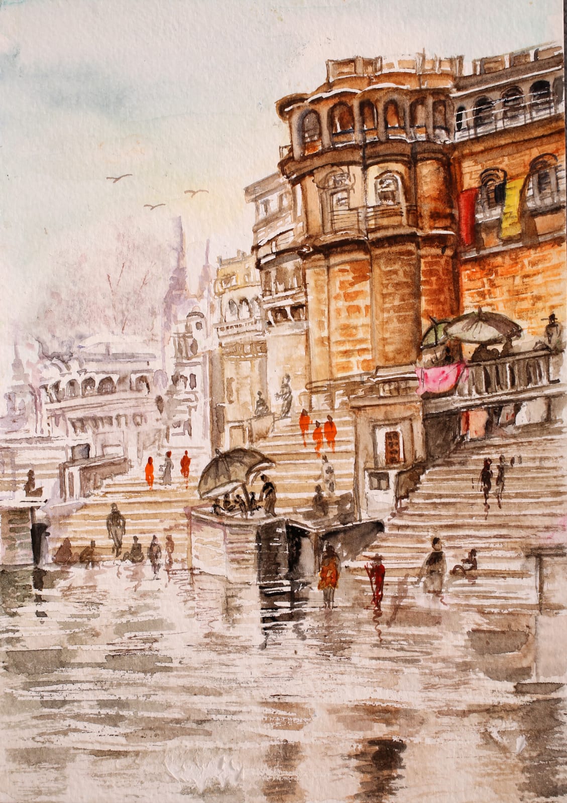 Wet ghat steps reflecting sandstone buildings, with umbrellas and saffron-robed figures climbing.