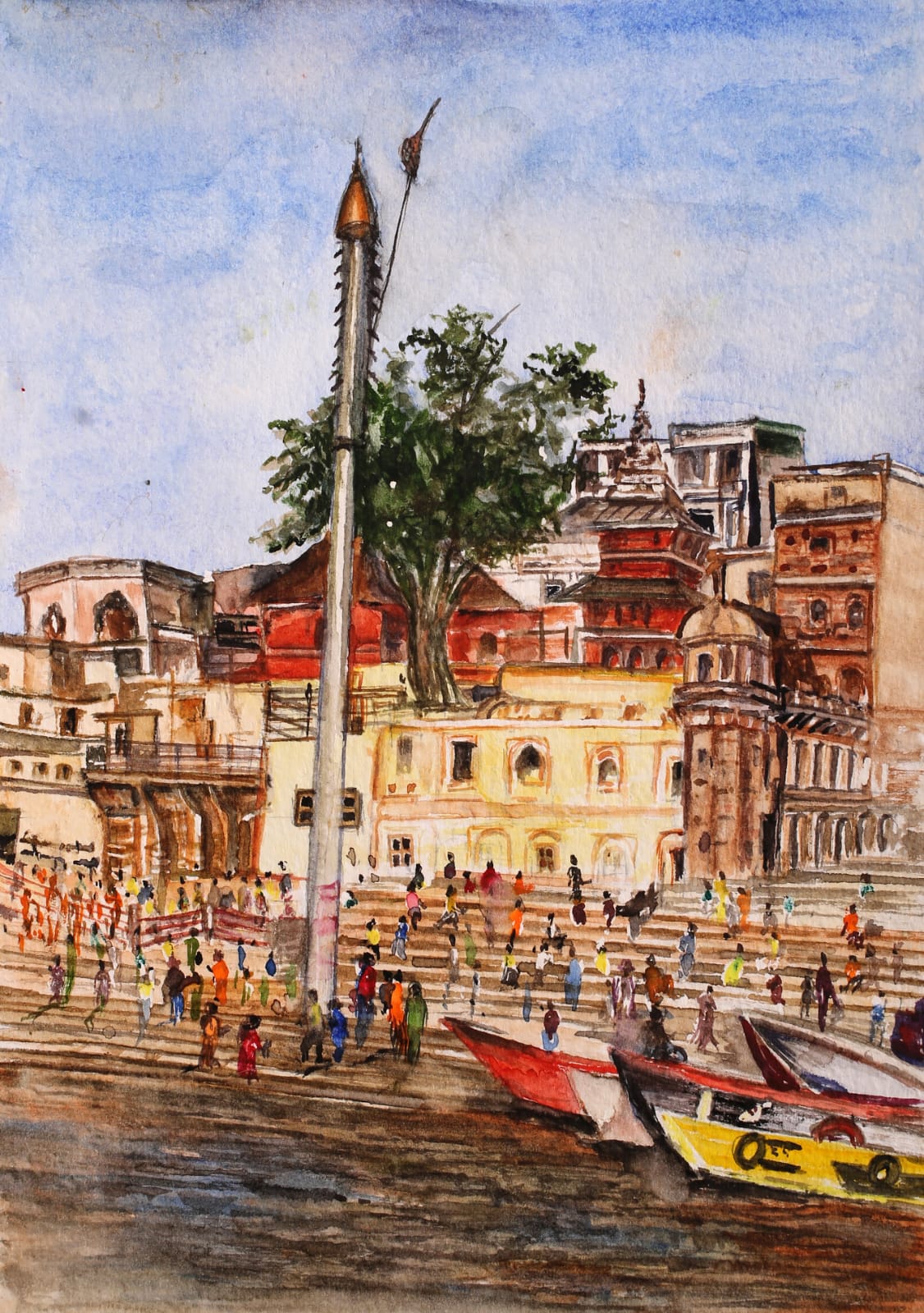 Crowds on the Varanasi ghat steps beside a tall pole, with temples behind and red and yellow boats at the water.